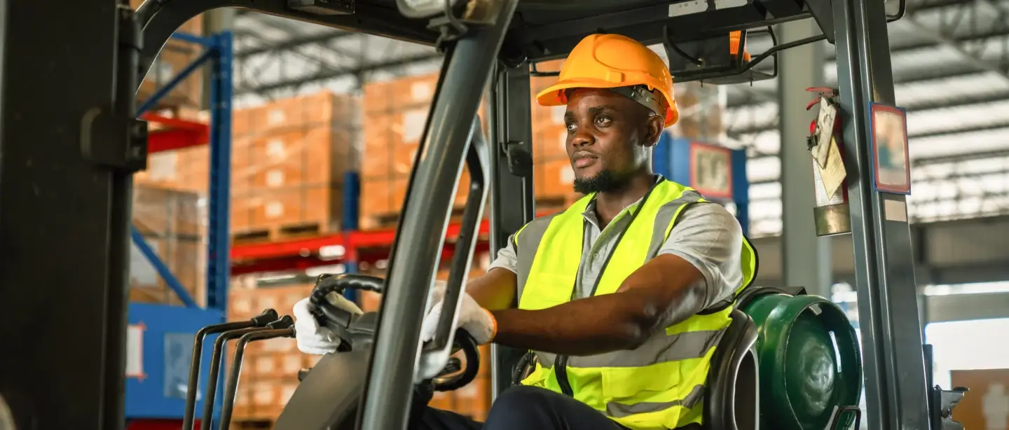 A man using driving a forklift with a helmet and a hi-vis on