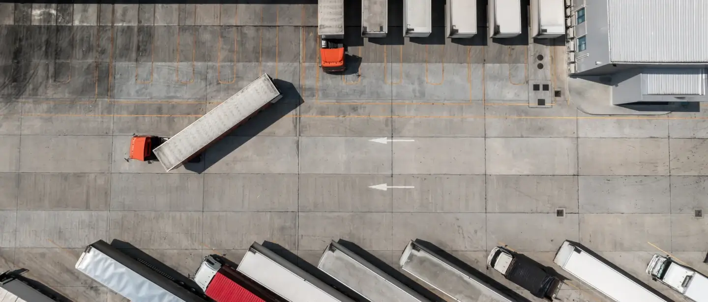 HGV's lined up parked in a warehouse from a birds eye view. One truck is leaving