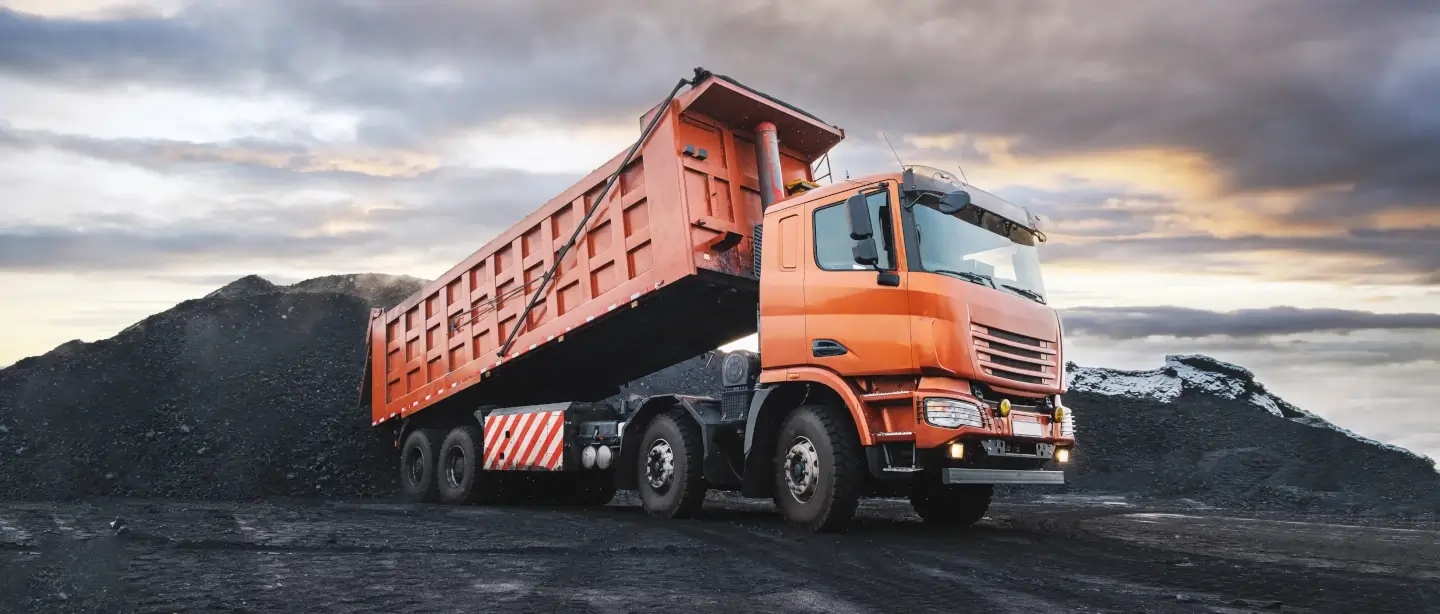 Orange rear dumper truck dumping material into a site