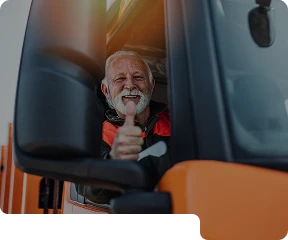 Man sitting in the front seat of a HGV truck looking out the window smiling, giving a thumbs up.
